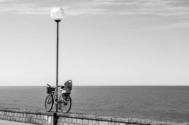 Sahildeki ışık sütuna bağlı bir bisiklet. Arka planda deniz var.