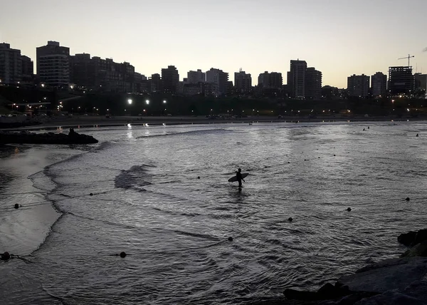 Bir sörfçü gün batımında Arjantin 'in Mar del Plata plajında denize giriyor.