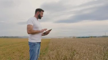 Buğday tarlasında tablet bilgisayarlı erkek çiftçi yürür ve buğday kalitesini kontrol eder..