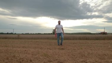 Tarım. Bir tarım uzmanı buğday tarlasında bir tabletle ayakta duruyor, arka planda bir kombine çalışıyor. Bir biçerdöver çiftçinin tarlasında buğday biçer..