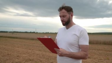 Not almak için tableti olan bir çiftçi arka planda çalışan çiftliklerin yanında duruyor. İşletme tarım kavramı. Modern tarım.