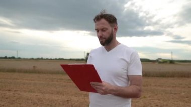 Not almak için tableti olan bir çiftçi arka planda çalışan çiftliklerin yanında duruyor. İşletme tarım kavramı. Modern tarım.