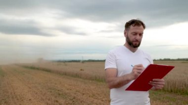 Not almak için tableti olan bir çiftçi arka planda çalışan çiftliklerin yanında duruyor. İşletme tarım kavramı. Modern tarım.