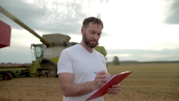 Farmer Tablet Taking Notes Stands Field Next Combines Working Background — Stock Video