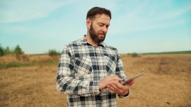 農場の農民アゴノミスト 小麦畑でタブレットを見ている農民 タブレットを手に持った農学者 農家経営者は有機農作物をチェックする エコカルチャーファーム — ストック動画