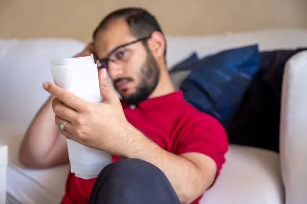 man is frustrated from the living costs holding his bill and sitting in front of the couch