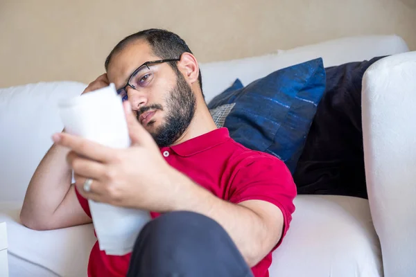 man is frustrated from the living costs holding his bill and sitting in front of the couch