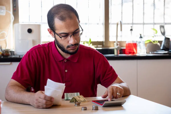 man sitting in the kitchen and calculating the costs of living feeling frustrated