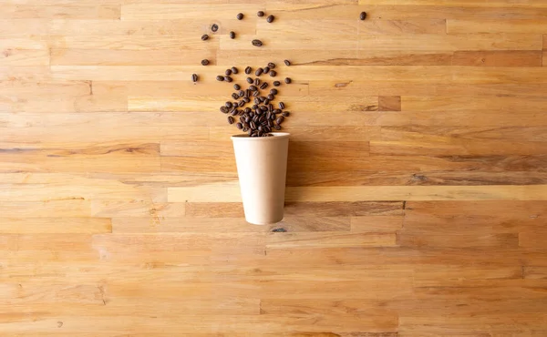 paper cup of coffee nature friendly on wooden background from top view with coffee beans spilled out