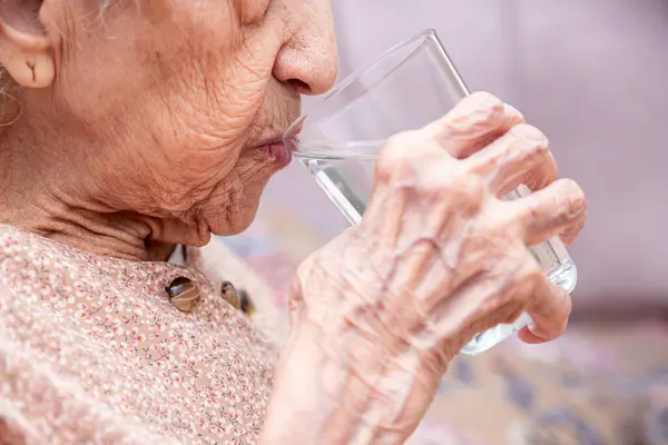 Old woman drinking water from glass cup