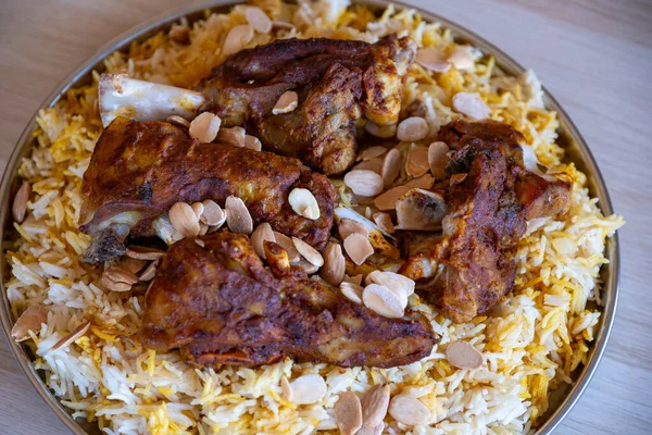 Plate of meat and rice topped with almonds on wooden table with top view