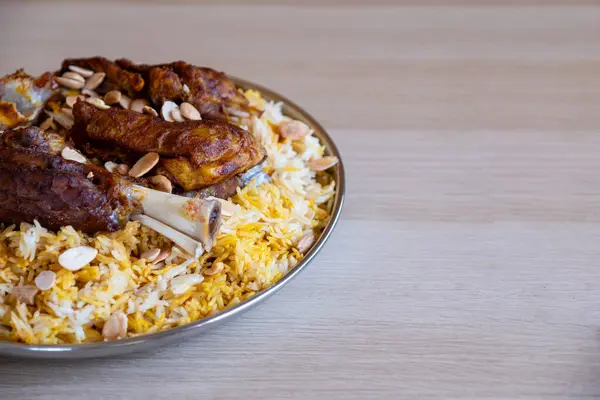 Plate of meat and rice topped with almonds on wooden table with top view