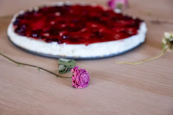 Cold cheesecake with cherry jelly and roses around it served on wooden background with green throw and antique forks