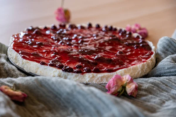 Cold cheesecake with cherry jelly and roses around it served on wooden background with green throw and antique forks