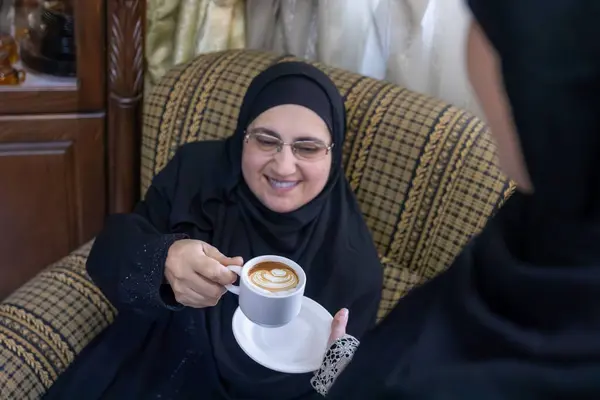 Arabic woman wearing hijab show hospitality for older woman serving her with arabic coffee