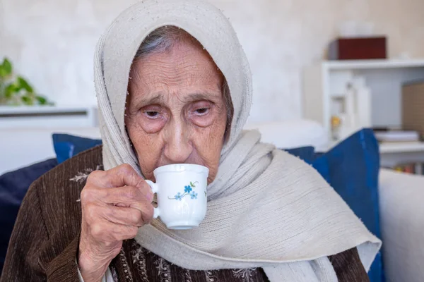 old woman holding cup of coffee drinking  it in living room