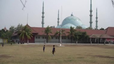 Tangerang, Banten. 14 Ekim 2023 - çocuklar öğleden sonra futbol oynuyorlar, arka plan caminin açık gökyüzü olan kubbesi ve minaresi. 