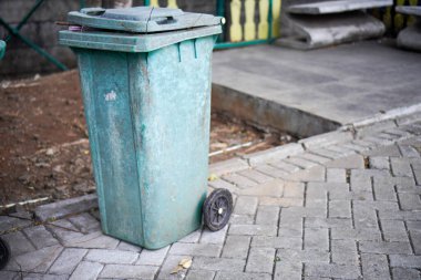 Yeşil çöp tenekeleri yolun kenarında. Rengi solmaya başlayınca yıpranmış görünüyor.. 
