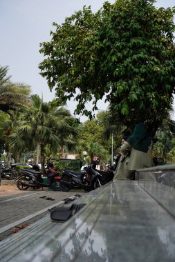 Tangerang, Banten. 14 Ekim 2023. Caminin avlusunda oturan kadın, yandan geniş bir açıyla görülüyor..