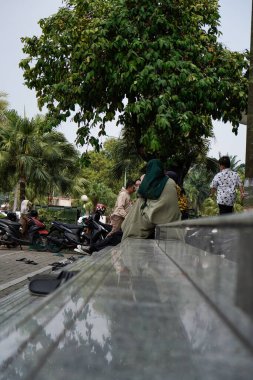 Tangerang, Banten. 14 Ekim 2023. Caminin avlusunda oturan kadın, yandan geniş bir açıyla görülüyor..