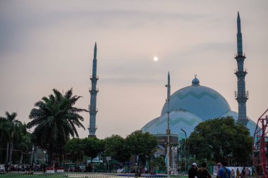 Her iki tarafında minareler olan güzel bir cami. Güneş batmak üzereyken gökyüzü arkaplanı. Önden geniş bir açıyla görülüyor. 