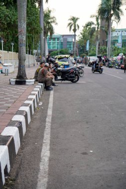 Tangerang, Banten. 14 Ekim 2023, Satpol polisi yol kenarında rahat bir şekilde oturuyor, geniş bir açıdan görülüyor.. 