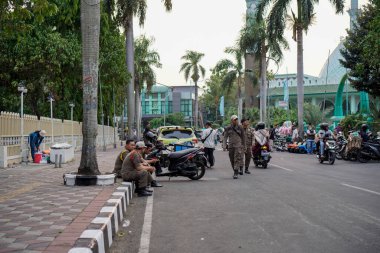 Tangerang, Banten. 14 Ekim 2023, Satpol polisi yol kenarında rahat bir şekilde oturuyor, geniş bir açıdan görülüyor.. 