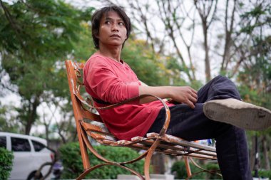 Kırmızı gömlekli bir Cava 'lı, bankta oturuyor, arka planda dikiliyordu. Düşük açılı bir bakış açısı vardı.. 