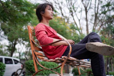 Kırmızı gömlekli bir Cava 'lı, bankta oturuyor, arka planda dikiliyordu. Düşük açılı bir bakış açısı vardı.. 