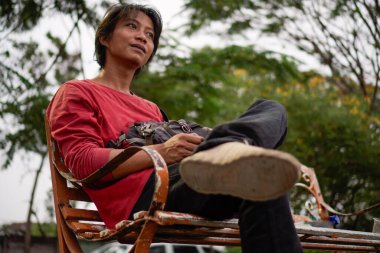 Kırmızı gömlekli bir Cava 'lı, bankta oturuyor, arka planda dikiliyordu. Düşük açılı bir bakış açısı vardı.. 