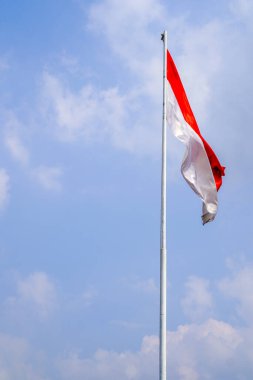 Bulutlarla dolu bir gökyüzünün arka planında kırmızı ve beyaz bir bayrak dalgalanıyor.. 