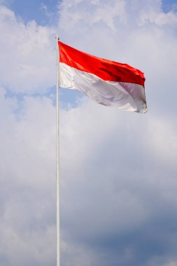 Bulutlarla dolu bir gökyüzünün arka planında kırmızı ve beyaz bir bayrak dalgalanıyor.. 