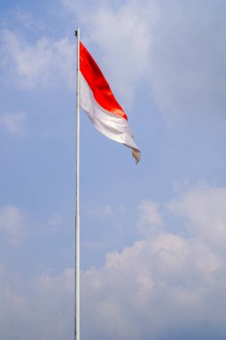 Bulutlarla dolu bir gökyüzünün arka planında kırmızı ve beyaz bir bayrak dalgalanıyor.. 