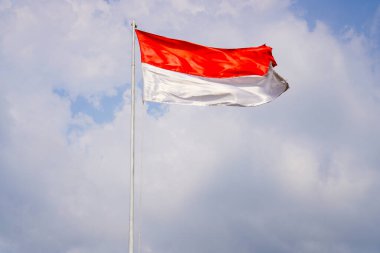 Bulutlarla dolu bir gökyüzünün arka planında kırmızı ve beyaz bir bayrak dalgalanıyor.. 