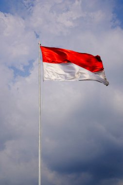 Bulutlarla dolu bir gökyüzünün arka planında kırmızı ve beyaz bir bayrak dalgalanıyor.. 