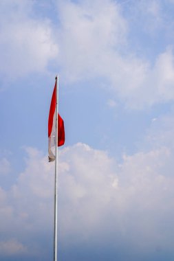 Bulutlarla dolu bir gökyüzünün arka planında kırmızı ve beyaz bir bayrak dalgalanıyor.. 