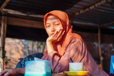 Başörtüsü takan bir kadının güzel görünüşü avuçlarında çenesiyle bir kafede oturuyor. 