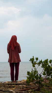 Sahilde durup okyanusa bakan başörtüsü takan bir kadının dikiz görüntüsü. 