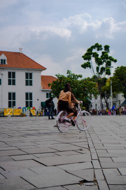Eski Jakarta kenti, 19 Aralık 2023 - Jakarta eski şehrinde bisiklet süren turistler ve arka planda tarihi binalar 