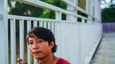 Kırmızılı adam parmaklıkları tutuyordu. Düşünceli bir ifadeyle..