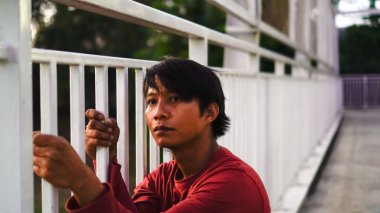 Kırmızılı adam parmaklıkları tutuyordu. Düşünceli bir ifadeyle..