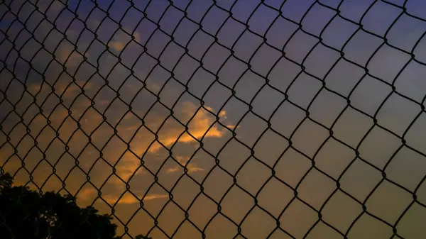 shot of the iron net fence against the background of an orange sky in the afternoon.