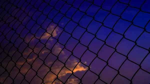 shot of the iron net fence against the background of an orange sky in the afternoon.