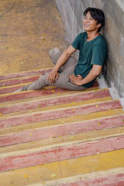 Yeşil elbiseli adam merdivenlerde oturuyordu. Yürümekten yorgun düşmüştü.. 