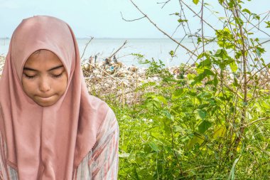 Başörtülü güzel bir kadın sahilde çimen arka planda oturuyor..