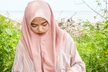 Başörtülü güzel bir kadın sahilde çimen arka planda oturuyor..