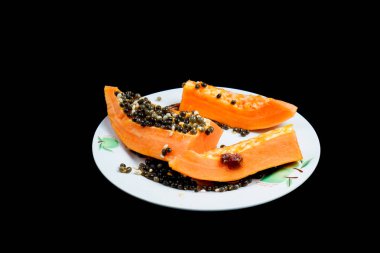 Siyah arka planda bir tabakta dilimlenmiş papaya meyvesi.