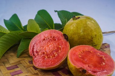 Guava izole edildi. Sarımsı yeşil derili kırmızı etli guava meyvesi koleksiyonu ve bambu hasırı ile beyaz arka planda izole edilmiş yapraklar..