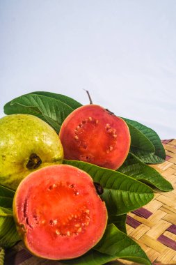 Guava izole edildi. Sarımsı yeşil derili kırmızı etli guava meyvesi koleksiyonu ve bambu hasırı ile beyaz arka planda izole edilmiş yapraklar..