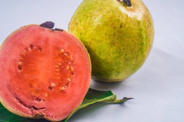Guava izole edildi. Beyaz arka planda izole edilmiş bir yaprağın üzerinde sarımsı yeşil derili kırmızı etli guava meyvesi koleksiyonu.